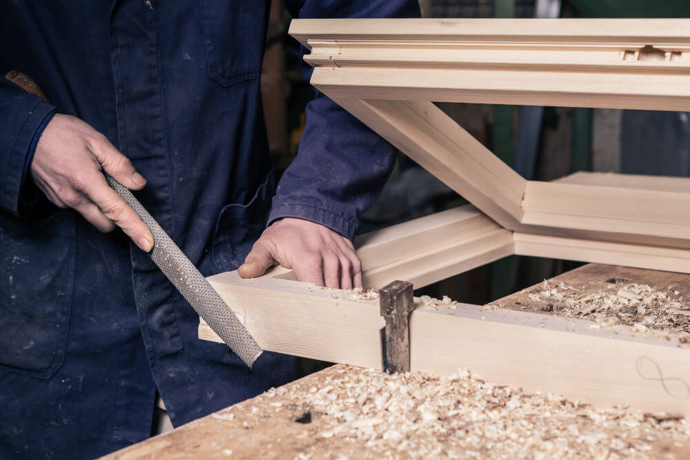 Carpintero rebaja madera con escofina en el banco del taller