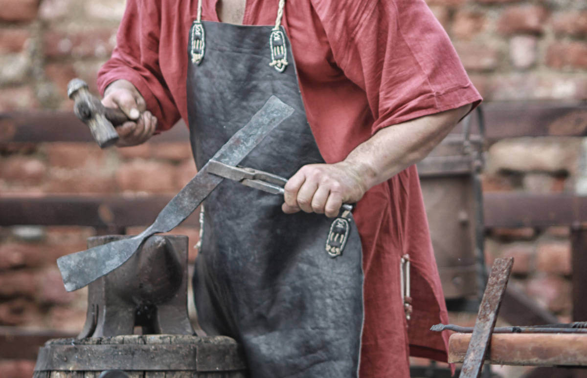 herrero trabaja acero en un yunque con martillo de bola