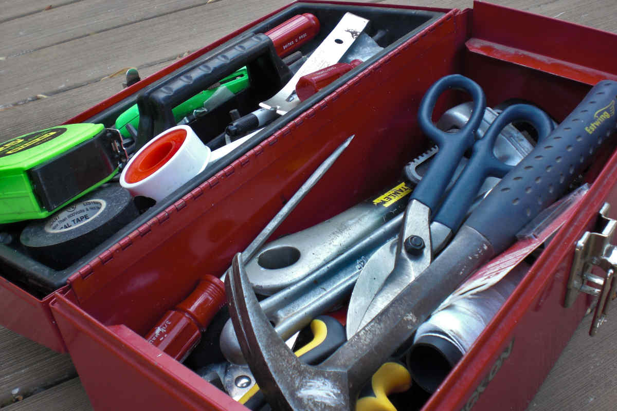 Caja de metal llena de herramientas de todo tipo y materiales esenciales: teflón, cinta aislante y cuerda.