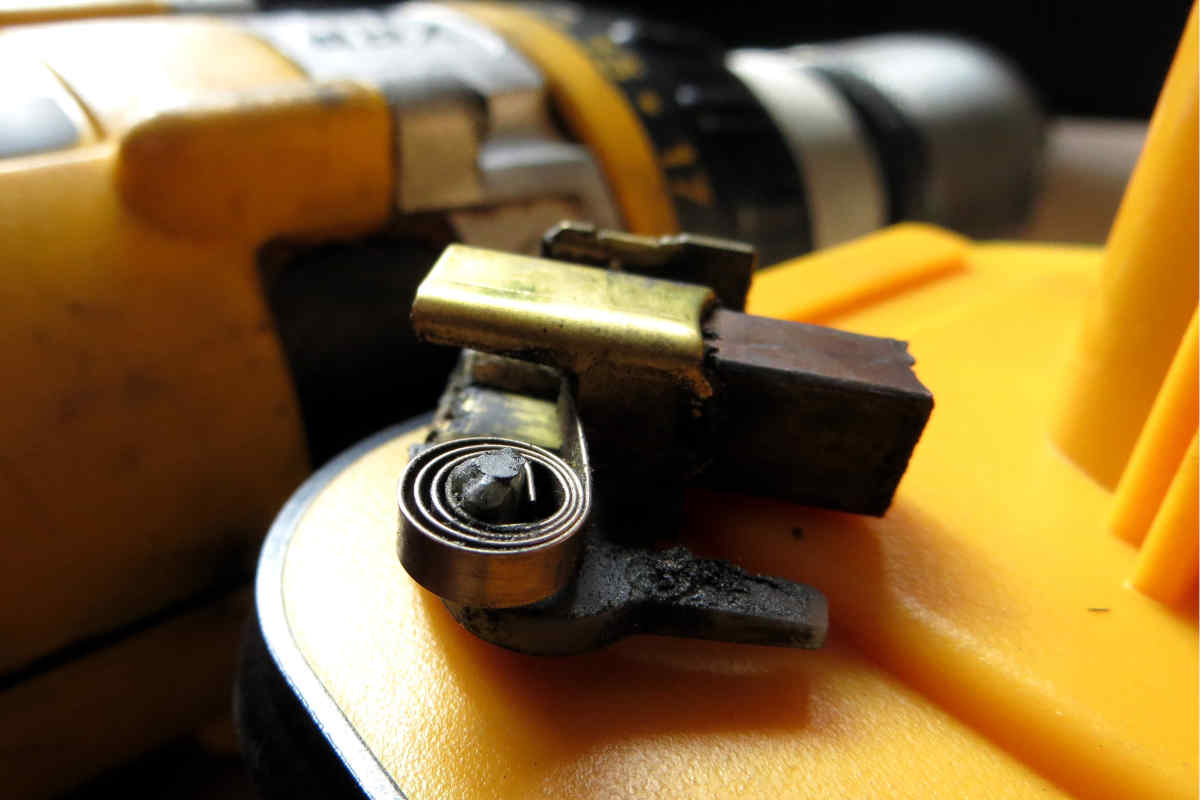 Escobilla de carbón gastada sobre la batería de de un taladro inalámbrico que se ve desenfocado al fondo.