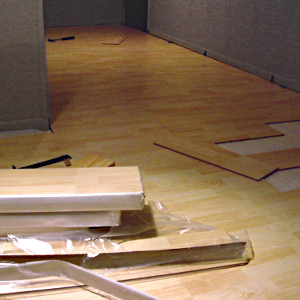 En primer plano cajas de tarima laminada; detrás, proceso de instalación del suelo flotante en una habitación.