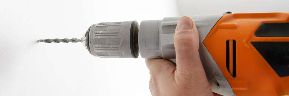 Un manitas usa un taladro percutor con cable para perforar una pared con broca de vidia.